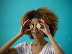 A young woman holding Bitcoins up to her eyes
